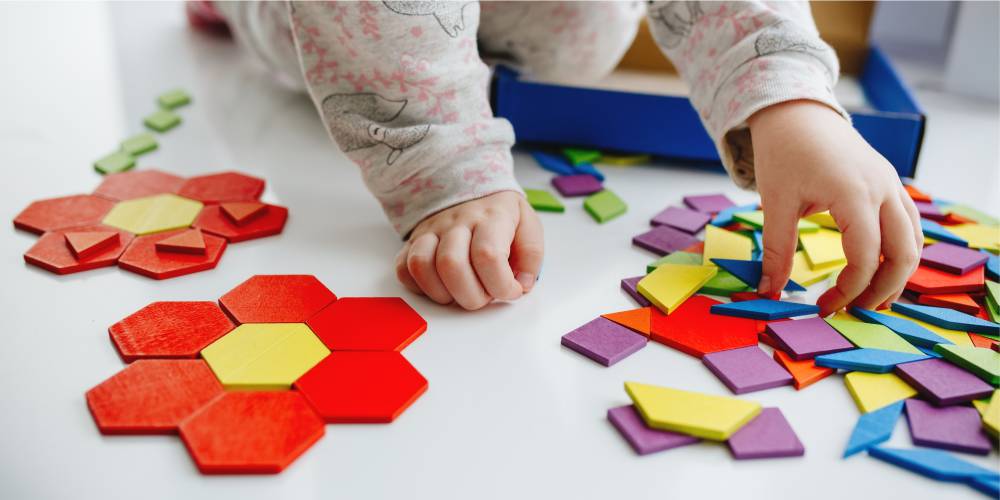 criança brinca com peças coloridas de tangram formando figuras