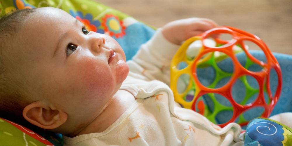 destaque para o rosto de bebê caucasiano, com bochechas rosadas, deitado sobre um tecido colorido