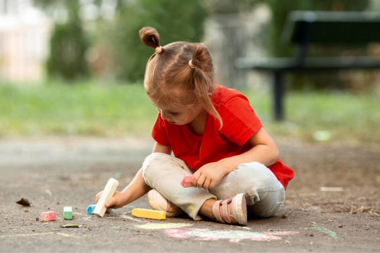 Criança sentada com as pernas cruzadas escrevendo sobre a calçada com giz