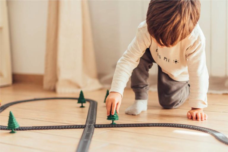 Criança brincando com árvores e trilhos de trem sobre o chão